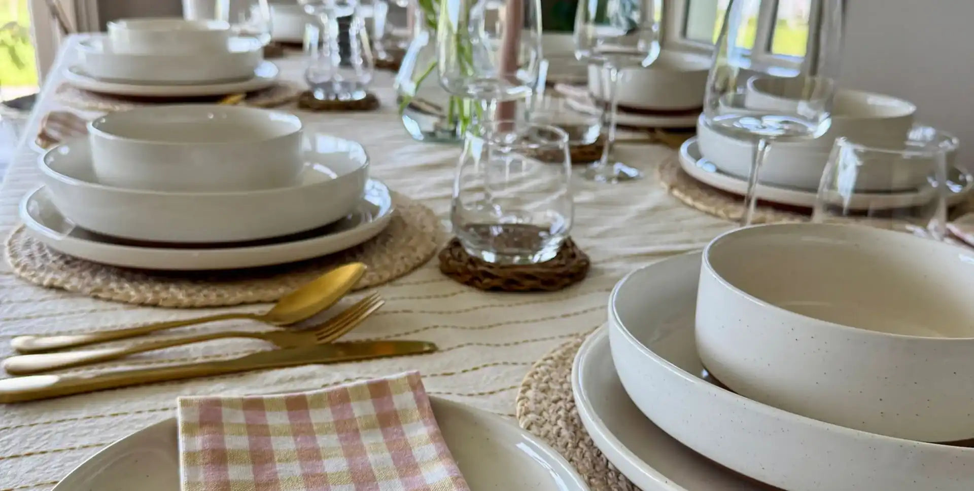 Ett bord dukat med neutrala tallrikar och gyllene bestick.