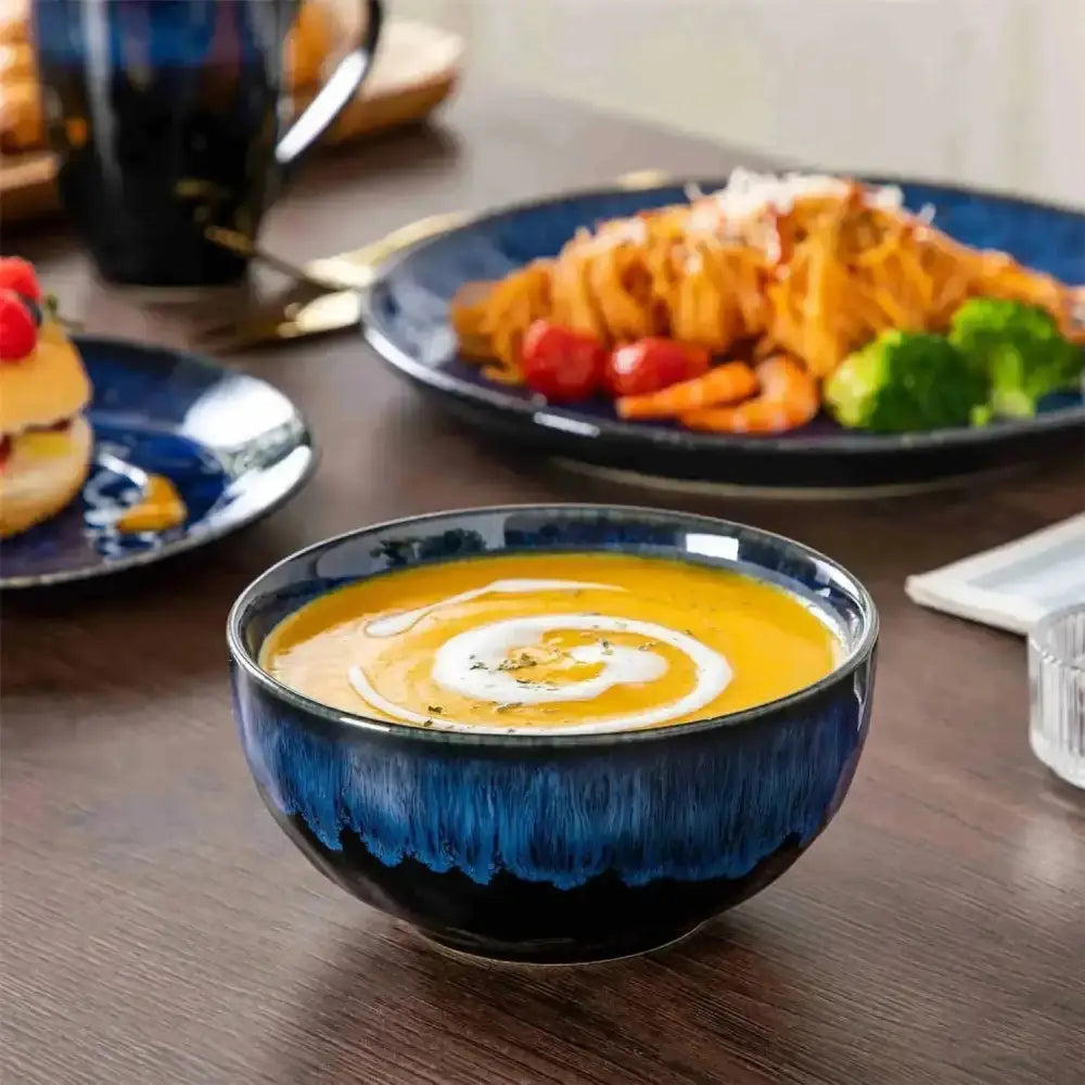 Deep blå keramisk skål med krämig orange soppa, garnerad med grädde och örter