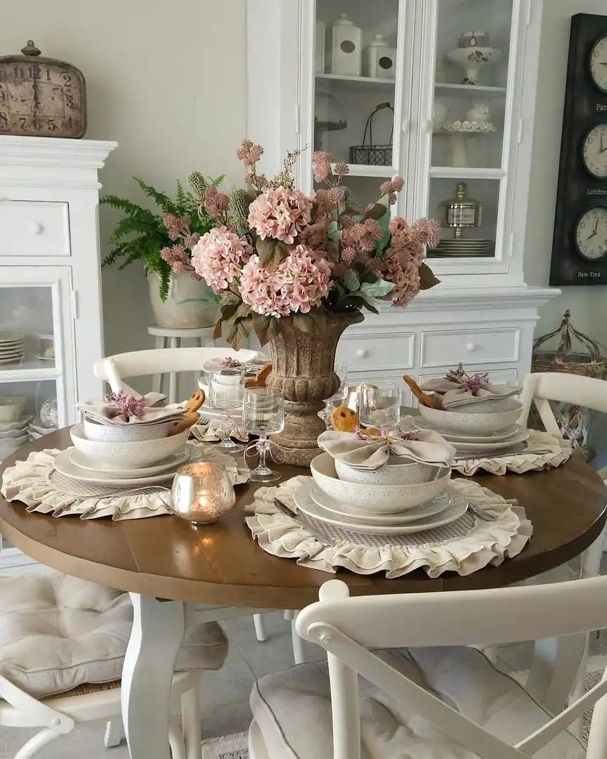 Ett runt träbord för fyra med vita stolar och ett blommönstrat mittpunkt.