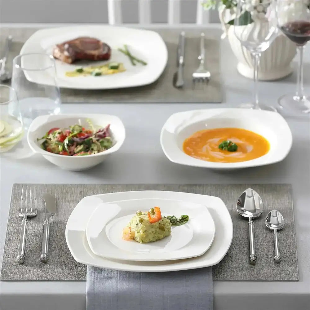Formell matbordssättning med vit kvadrat- och rundservis, bestick och olika rätter